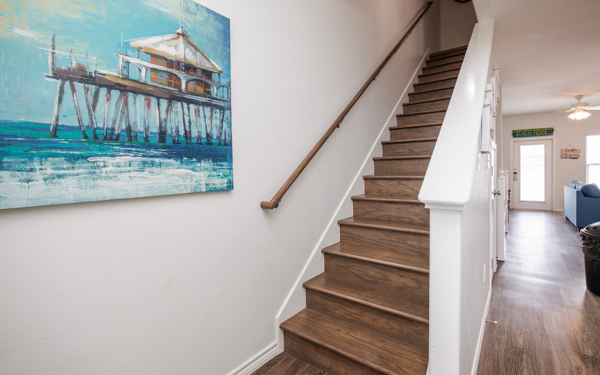 Step into your coastal retreat where ocean-inspired artwork welcomes you up beautiful hardwood stairs to your home away from home.