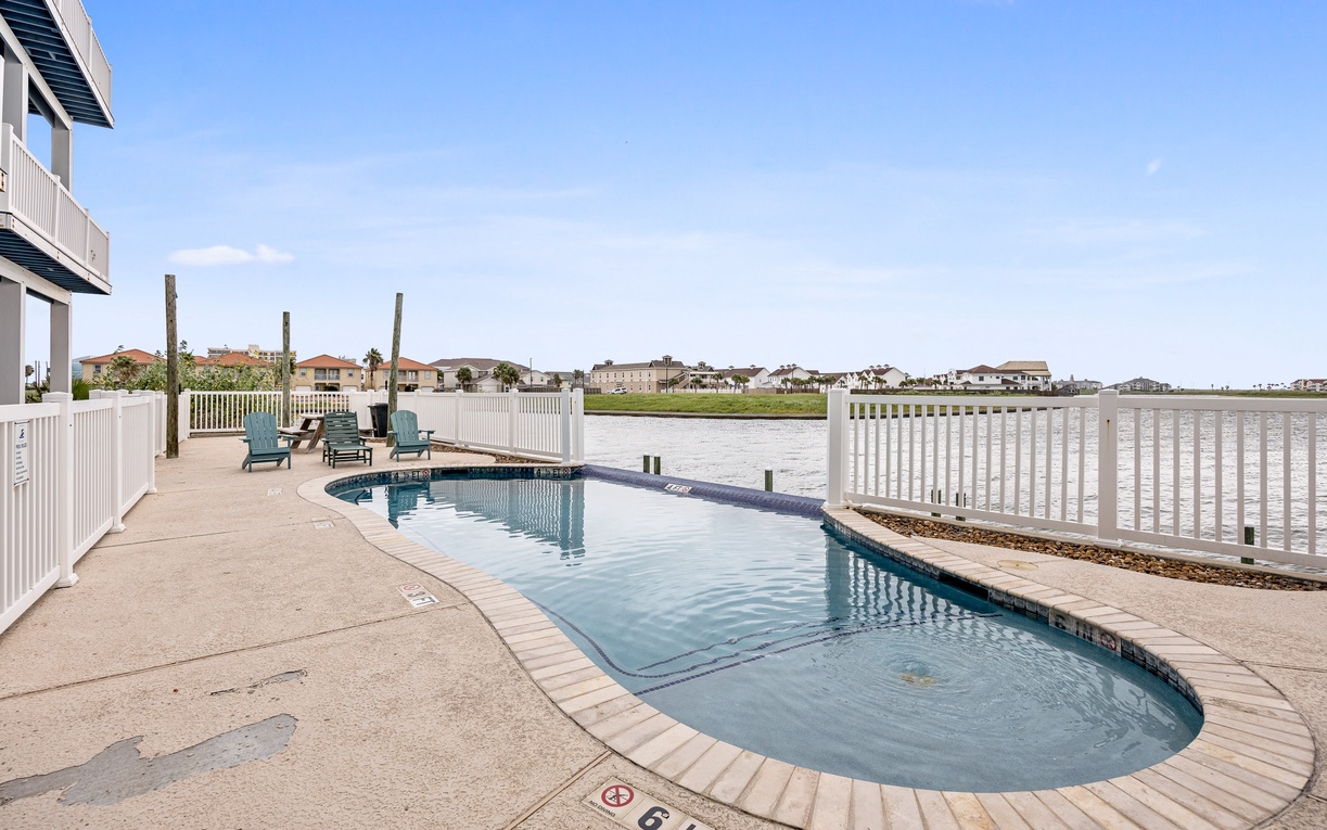 Waterfront pool deck with lounge chairs offers peaceful views across the water to neighboring homes.
