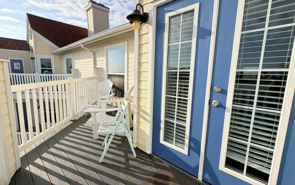 Step onto your private deck where white rocking chairs await under the coastal sky, perfect for morning coffee or evening relaxation.