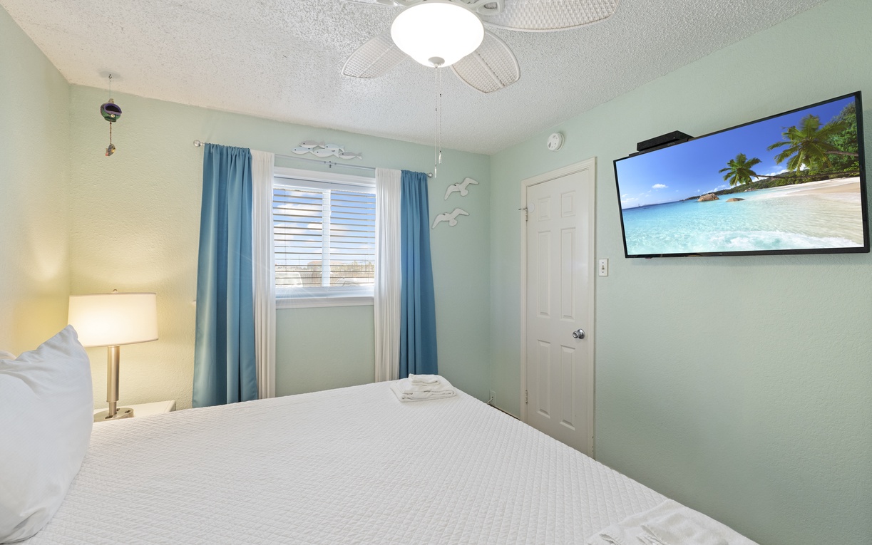 Sink into crisp linens under a cooling ceiling fan in your calming coastal retreat. A flat-screen TV awaits your favorite shows while soft lighting creates the perfect ambiance for relaxing after a day of adventure.