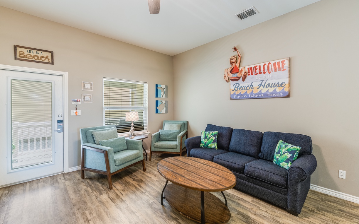 Sink into the plush navy sofa or mint green chairs in this welcoming living space, where coastal charm meets comfort for your perfect getaway.