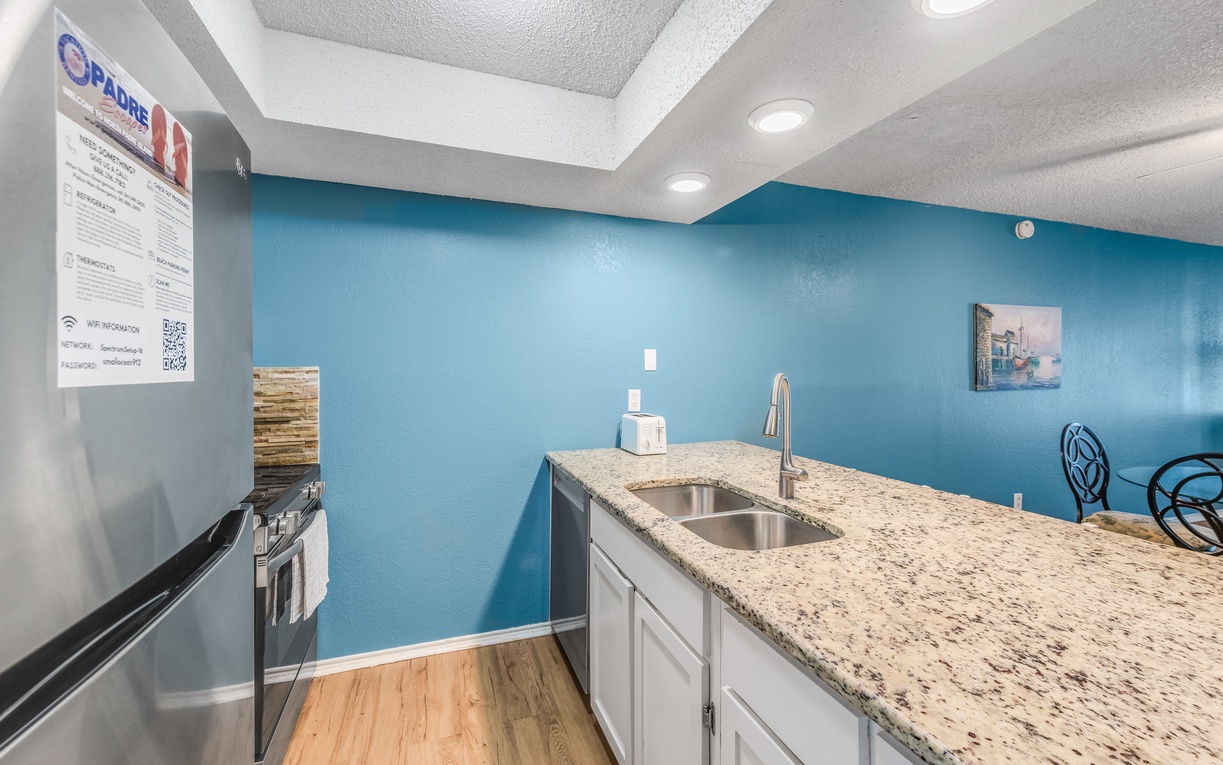 Prepare your favorite meals in this bright, fully-equipped kitchen featuring granite countertops, stainless steel appliances, and cheerful blue accent walls.