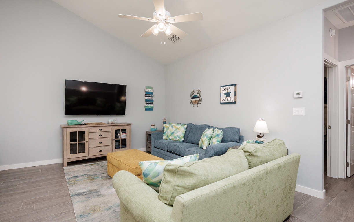 Relax in your spacious living room with comfortable seating, large TV, and coastal decor that creates the perfect home-away-from-home atmosphere.