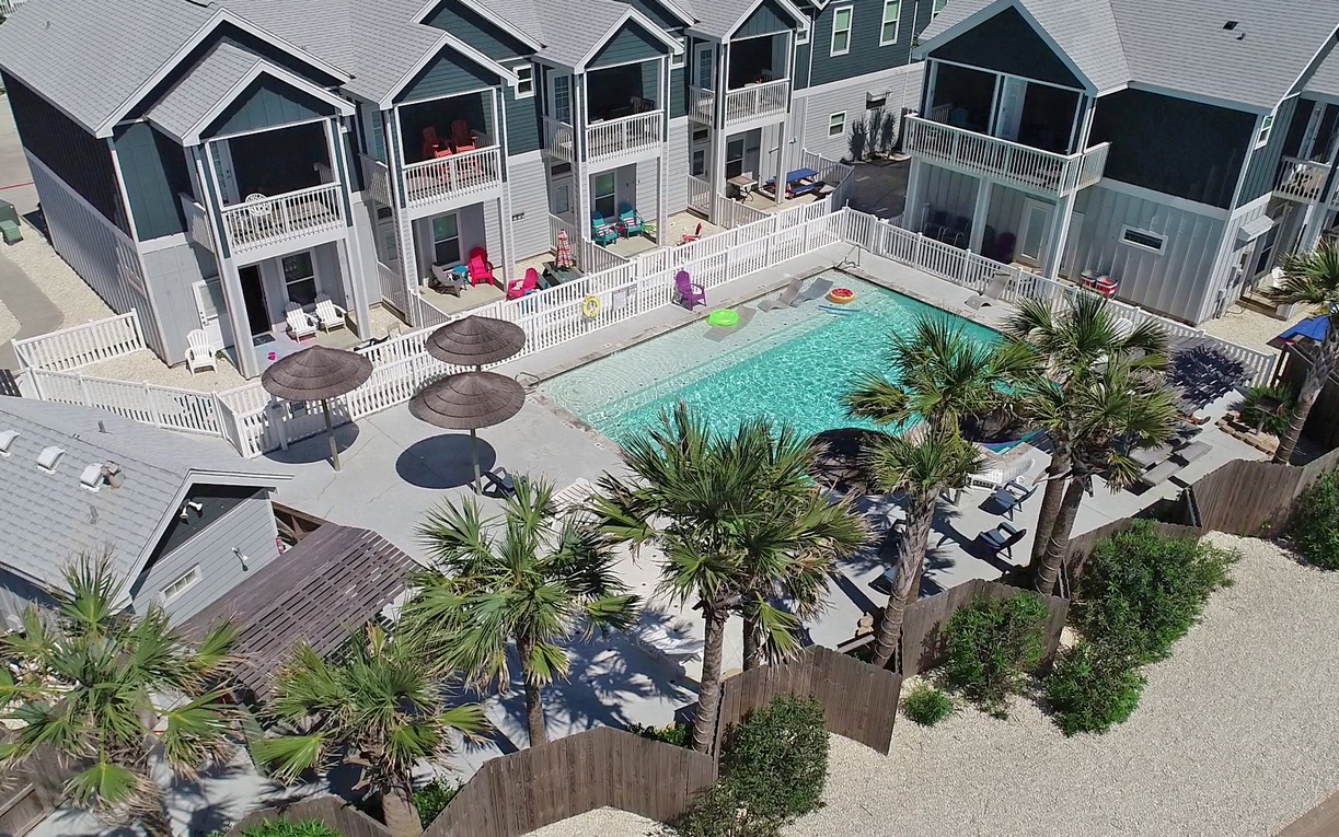 Aerial view of beachside vacation rental complex with shared swimming pool and tropical landscaping surrounded by coastal cottages.