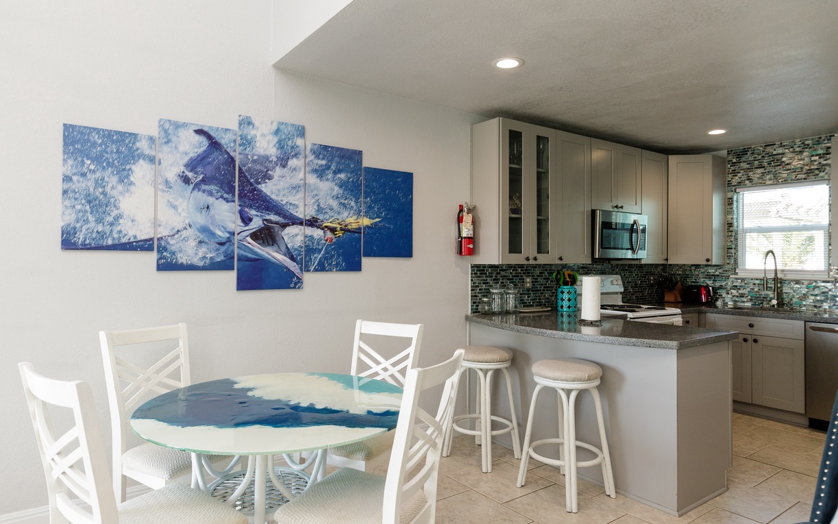 Your open-concept kitchen and dining space features modern appliances and coastal artwork, perfect for preparing meals together.