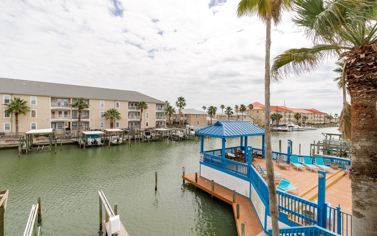 Waterfront resort community with tropical landscaping, boat docks, and covered marina pavilion surrounded by palm trees.