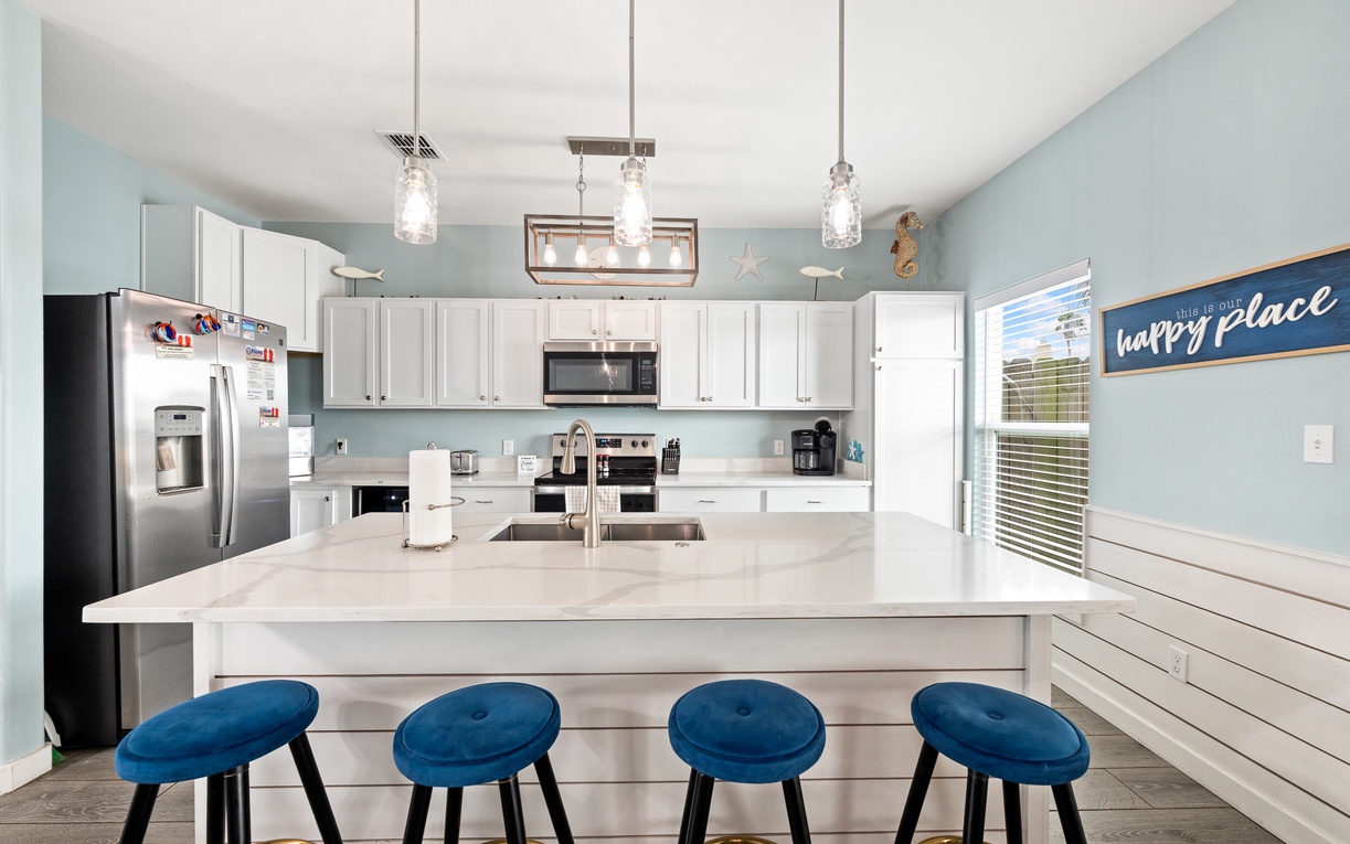 Your coastal-inspired kitchen welcomes you with soft aqua walls, white cabinetry, and charming beach décor—perfect for gathering around the island as you plan your day or share a meal together.