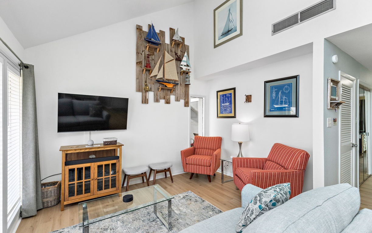 Relax in your nautical-themed living room with comfortable seating, modern TV, and charming coastal decor creating the perfect vacation atmosphere.