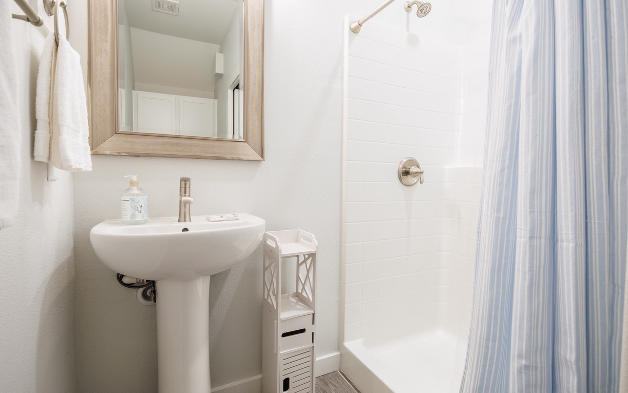 Step into your pristine private bathroom featuring a refreshing walk-in shower and elegant pedestal sink for your daily routines.