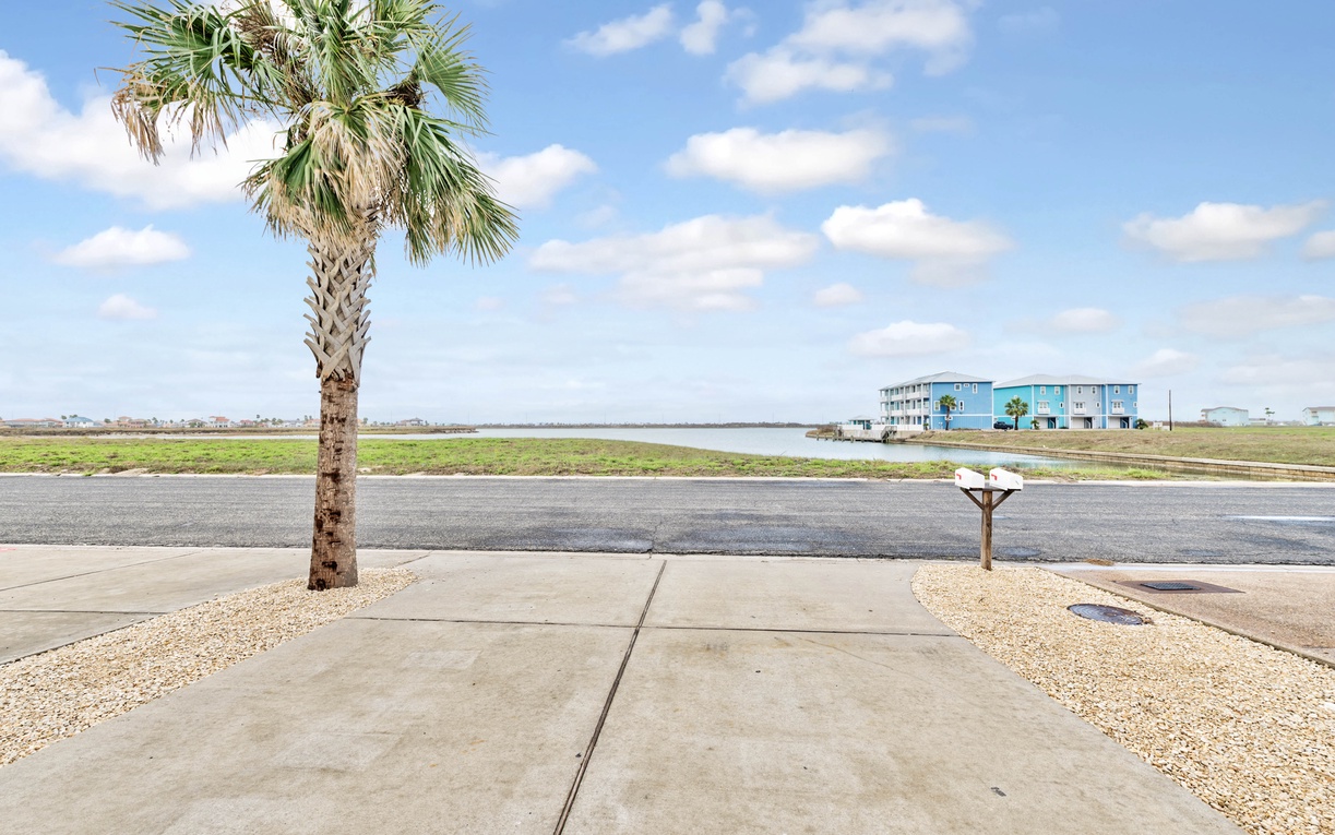 Coastal property with palm tree landscaping and water views across the street from colorful beach houses.