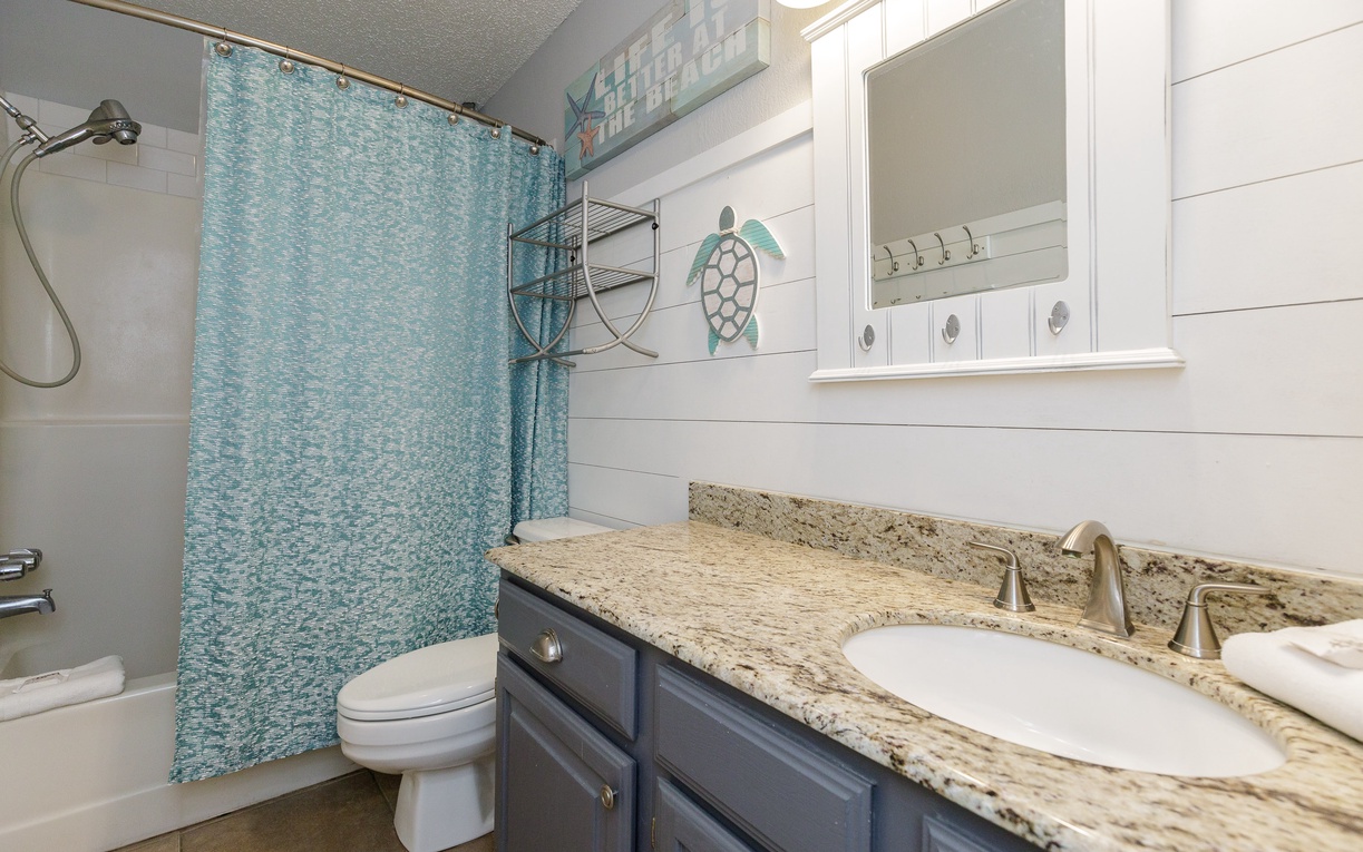 Refresh in your coastal-themed bathroom with granite counters, custom cabinetry, and charming sea turtle artwork that brings beachy vibes indoors.