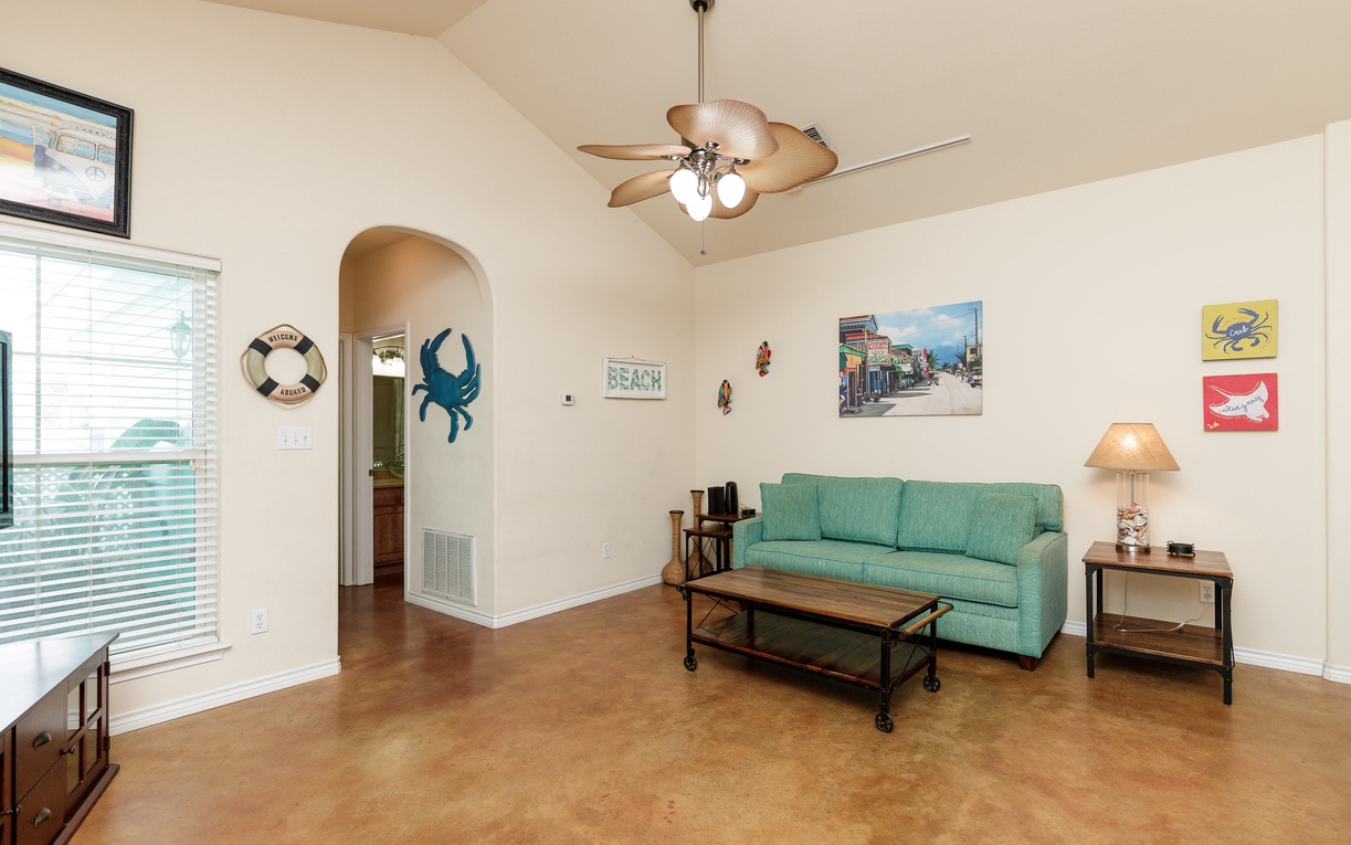 Relax in your coastal-themed living room with comfortable seating, tropical ceiling fan, and charming beach décor that sets the perfect vacation mood.