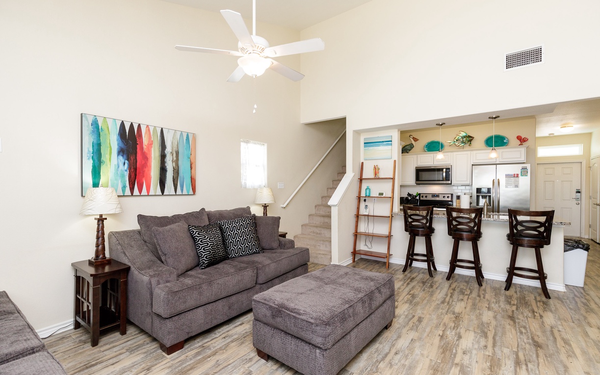 Relax in your spacious living room with cozy gray seating, modern art, and an open kitchen perfect for entertaining.