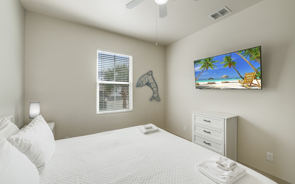 Drift off in your serene bedroom with coastal charm, complete with ceiling fan comfort and tropical dreams on the wall-mounted TV.
