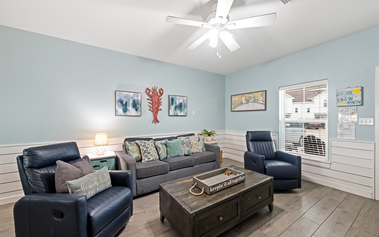Settle into your coastal-inspired living room, where soft blue tones and nautical touches create the perfect backdrop for your beachside retreat. Relax in the plush seating or catch a gentle breeze from the ceiling fan overhead.