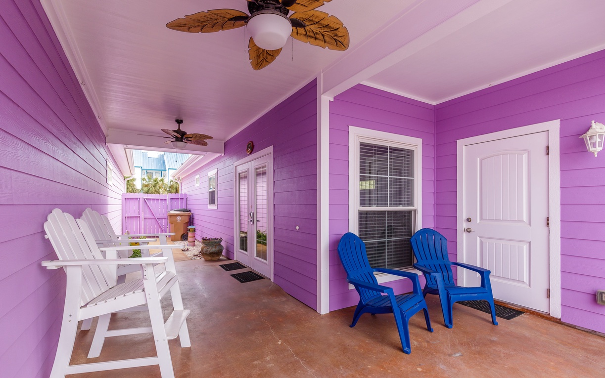 Step onto your vibrant covered porch where white chairs and bright blue seating invite you to unwind beneath tropical ceiling fans.