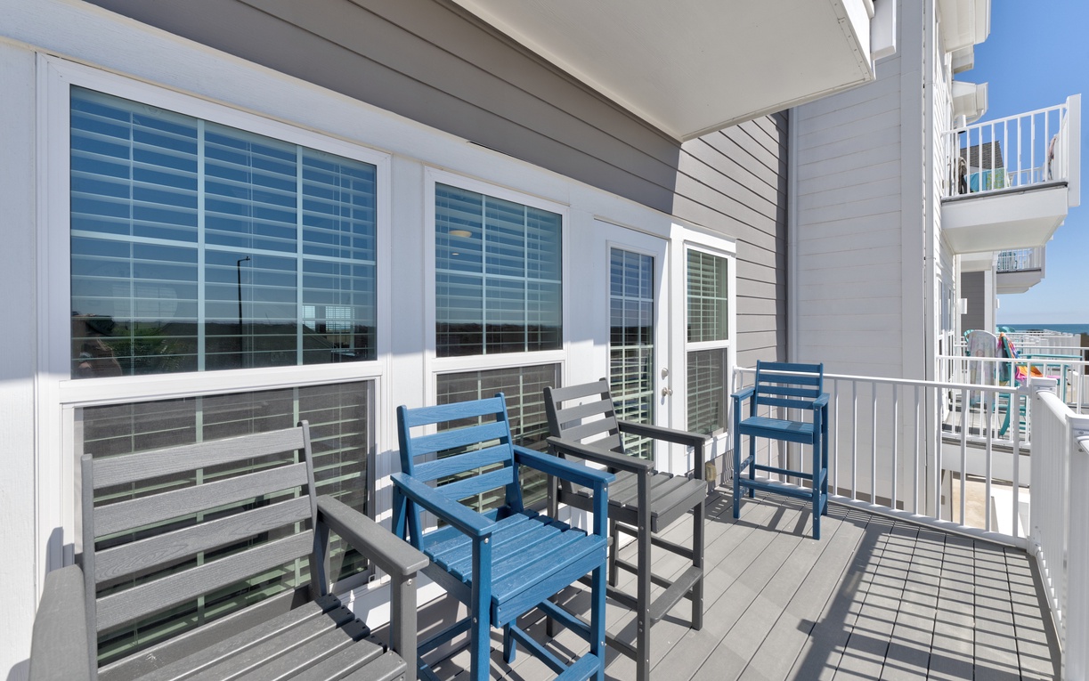 Step onto your private deck where blue chairs invite relaxation beneath ocean views and coastal breezes.