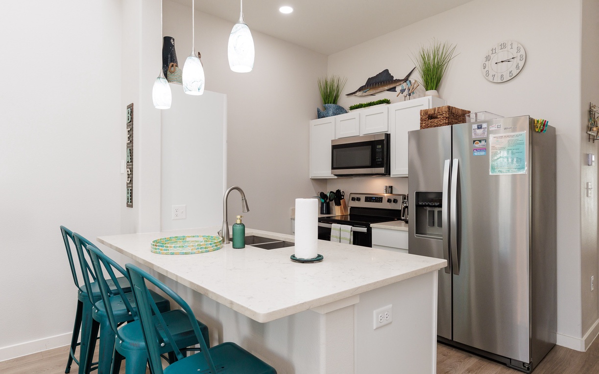 Your bright, modern kitchen features sleek white countertops, stainless steel appliances, and cheerful turquoise bar stools for casual dining.