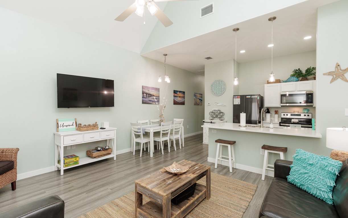 Relax in your spacious open-plan living area with coastal-themed decor, modern kitchen, and comfortable seating perfect for vacation gatherings.