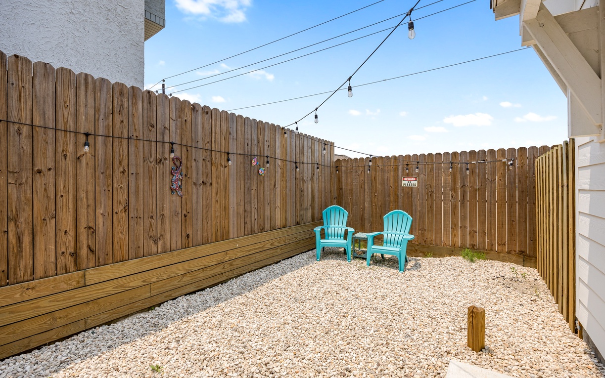 Your private backyard oasis features turquoise chairs under twinkling string lights, perfect for morning coffee or evening relaxation.