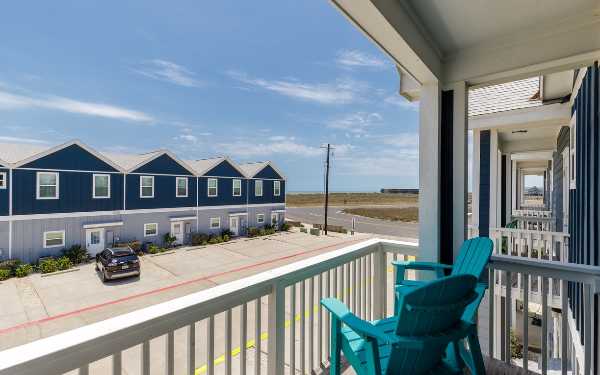Relax on your private balcony with turquoise chairs, taking in the coastal neighborhood views and open sky above.