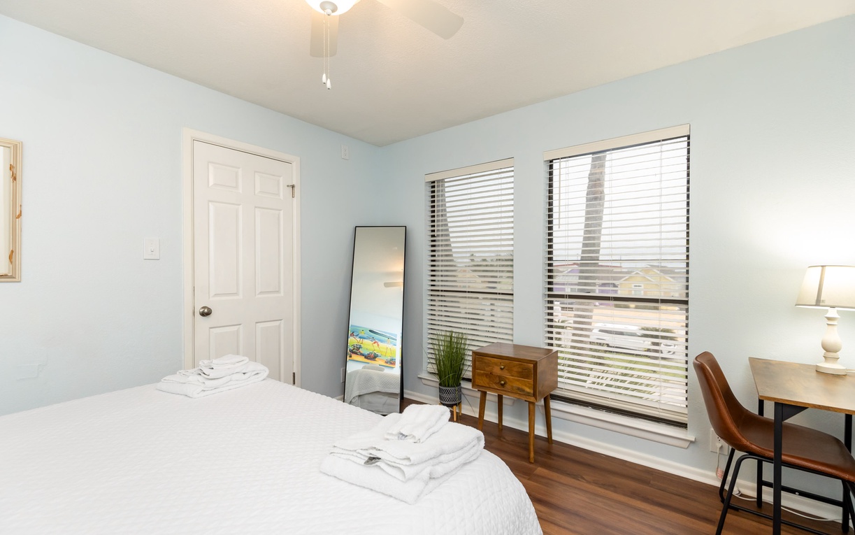 Sink into crisp white linens in your peaceful bedroom, where soft blue walls and warm hardwood floors create the perfect retreat for restful nights.
