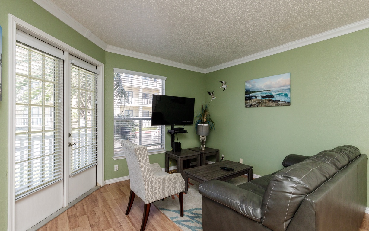 Relax in your peaceful living room with comfortable leather seating and entertainment center, perfectly positioned near patio doors for natural light.