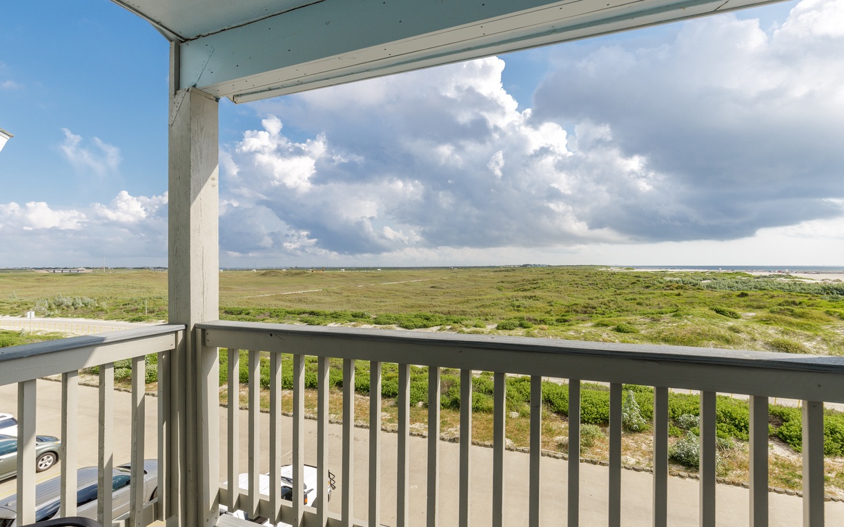 Sweeping natural landscape views stretch endlessly from this covered balcony overlooking green meadows and dramatic cloudy skies.