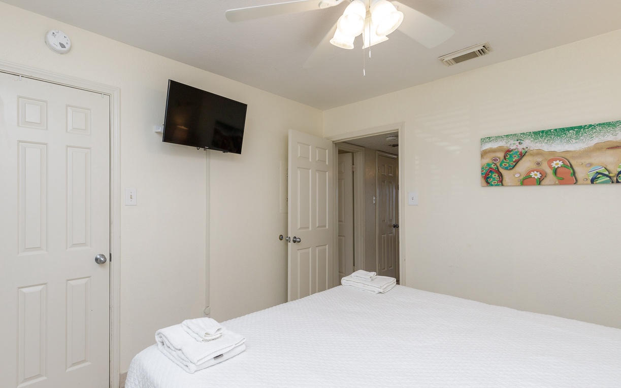 Unwind in your comfortable bedroom with fresh linens, ceiling fan, and wall-mounted TV for cozy evenings.