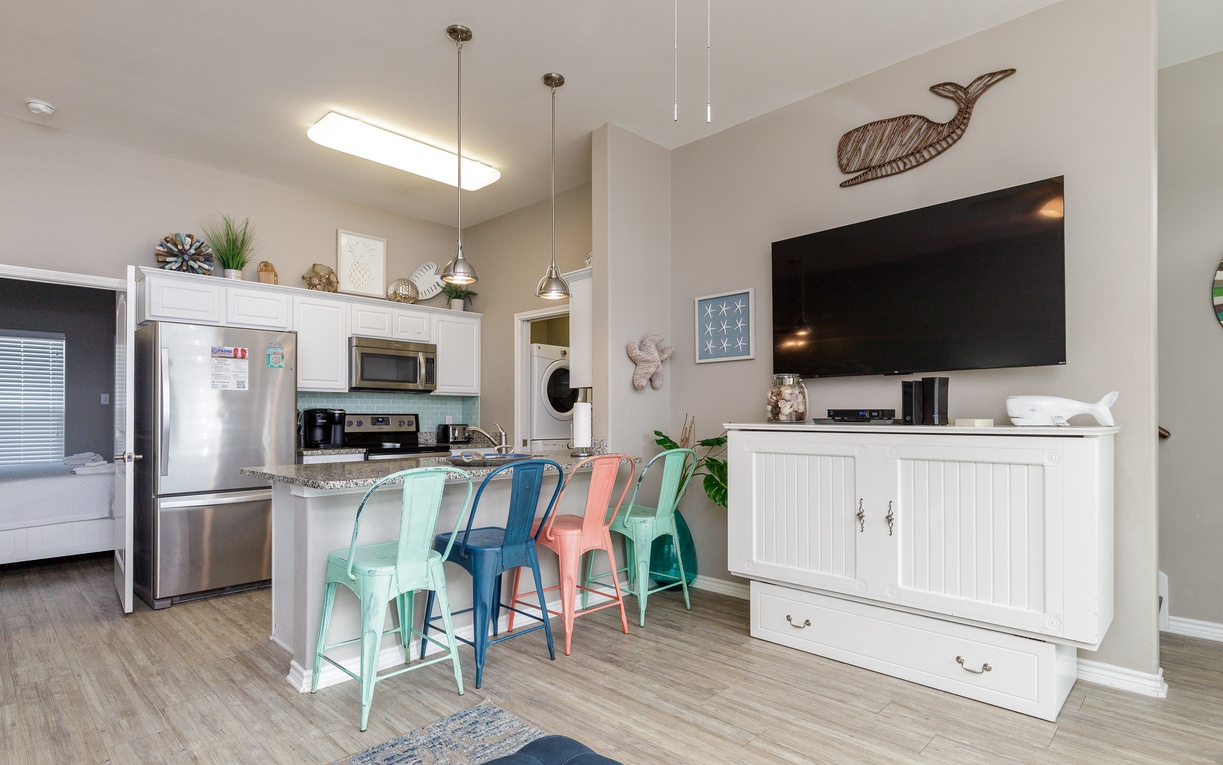 Bright open-concept space where your kitchen flows into the living area, featuring colorful bar stools and coastal charm for relaxed beachside dining.