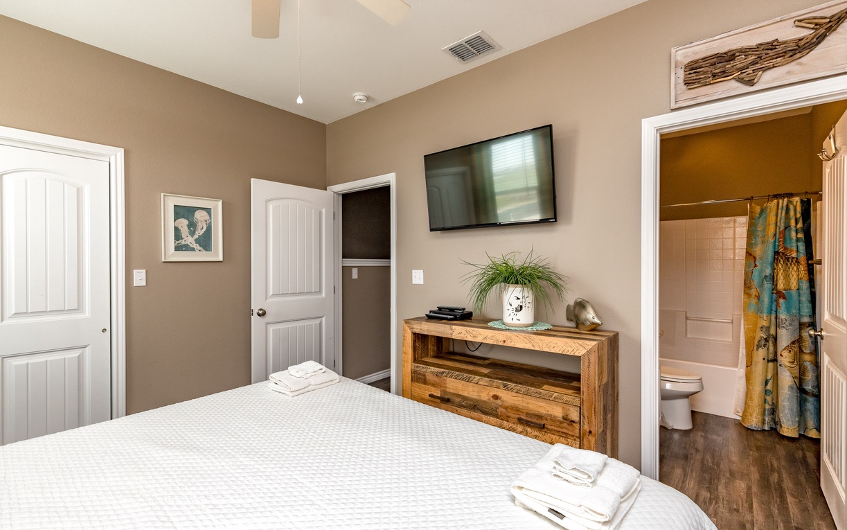 Unwind in your cozy bedroom featuring a comfortable bed, rustic entertainment center, wall-mounted TV, and convenient en-suite bathroom access.