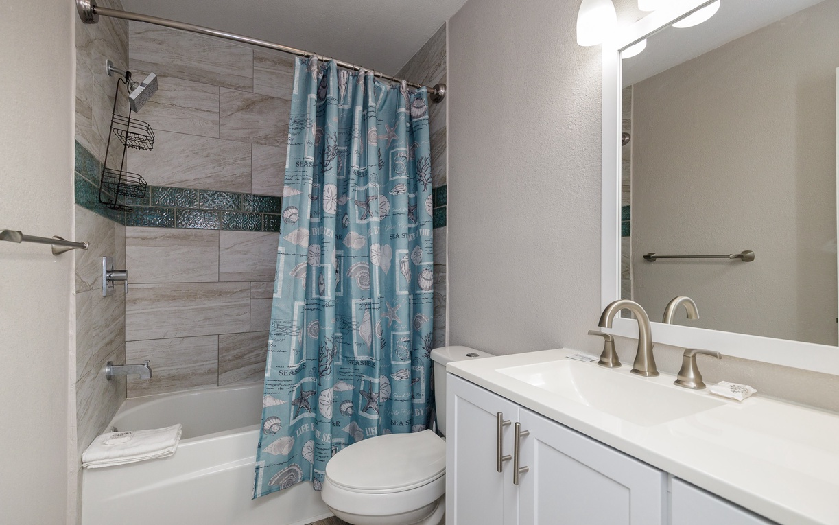 Unwind in your pristine bathroom featuring wood-look tile, ocean-themed accents, and everything you need for a refreshing shower or relaxing bath.