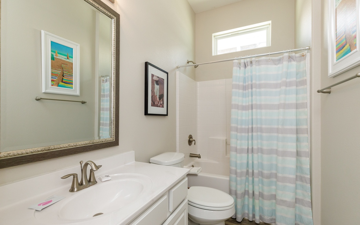 Your private bathroom features a refreshing shower-tub combo, elegant marble countertops, and cheerful coastal artwork to brighten your morning routine.
