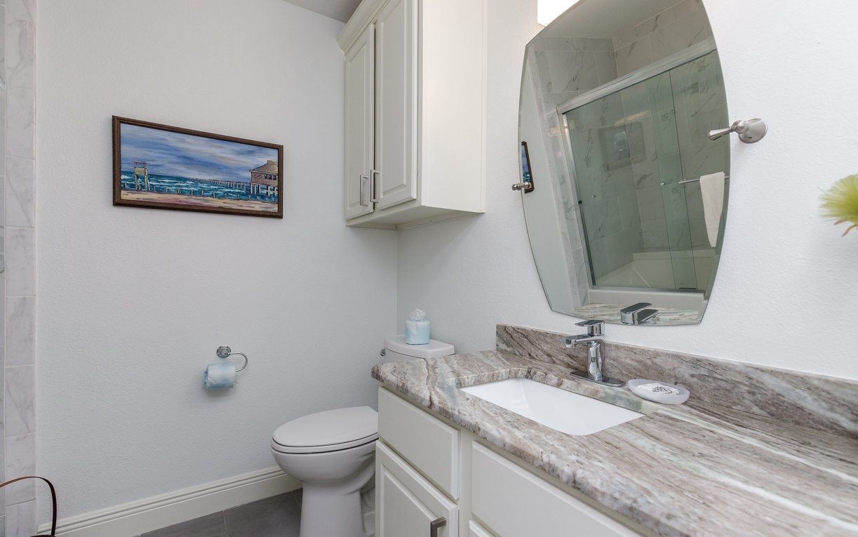 Refresh in your elegant bathroom with white cabinetry, marble countertops, and a spacious walk-in shower behind gleaming glass doors.