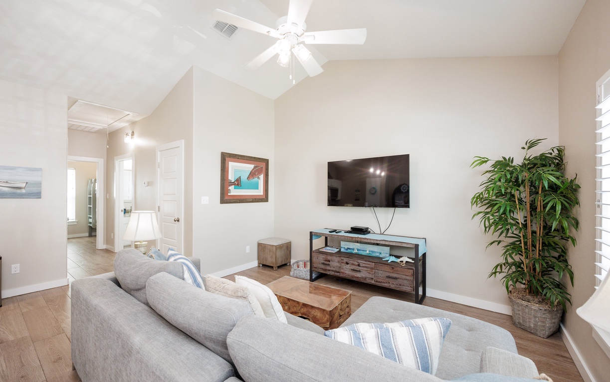 Settle into your bright living room with plush gray seating, modern entertainment setup, and tropical artwork creating the perfect space to unwind.