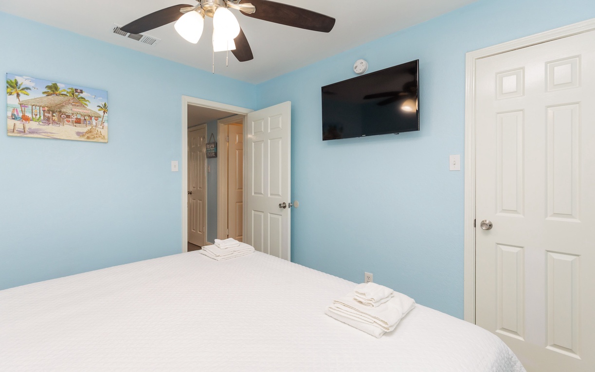 Unwind in your serene bedroom with coastal blue walls, ceiling fan for comfort, and wall-mounted TV for relaxation.
