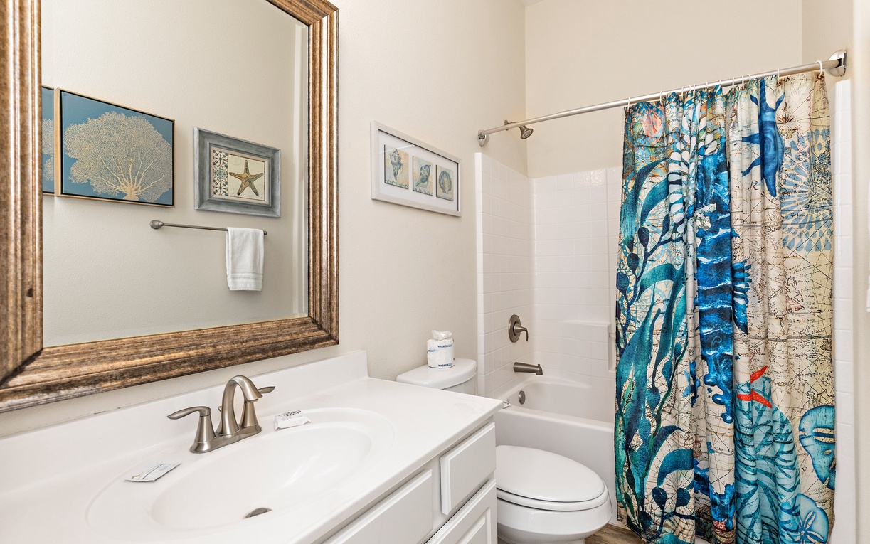 Unwind in your stylish bathroom featuring ocean-themed artwork and a refreshing tub-shower combo perfect for post-adventure relaxation.