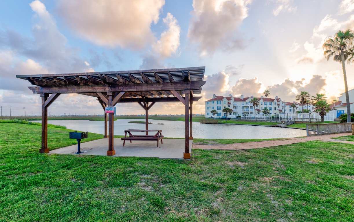 Waterfront gazebo with picnic table overlooking peaceful lagoon. Property buildings and palm trees frame this scenic outdoor space.