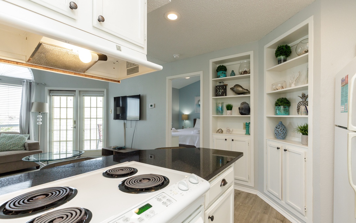Your coastal-inspired kitchen features granite countertops and built-in shelving displaying charming décor, creating a perfect space for preparing vacation meals.