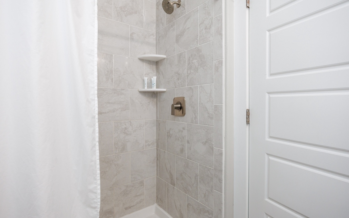 Step into your elegant marble-tiled shower with modern fixtures and convenient built-in shelving for all your essentials.