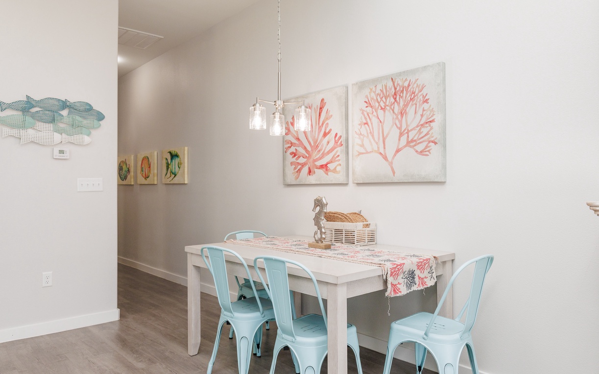 Gather around this charming coastal-themed dining area where your morning coffee tastes better surrounded by ocean-inspired art and cheerful turquoise chairs.
