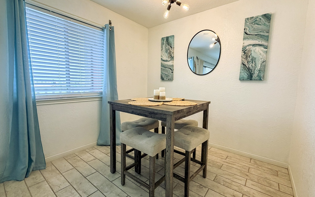Gather around your cozy dining table for intimate meals, with soft morning light filtering through blue curtains and calming ocean artwork.