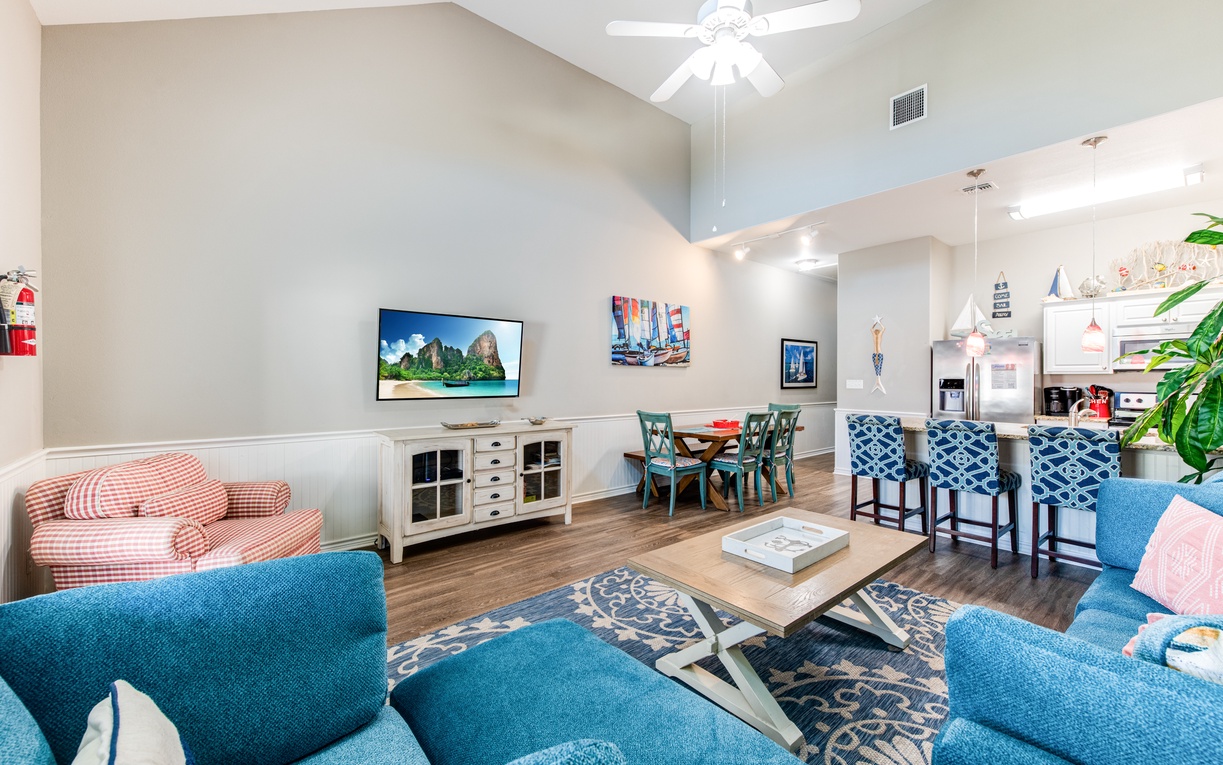 Relax in your bright open living space with soaring ceilings, cozy blue seating, and modern entertainment - perfect for unwinding after beach days.