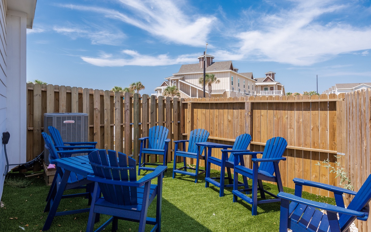 Relax in your private backyard oasis with bright blue Adirondack chairs on soft artificial turf, surrounded by privacy fencing.