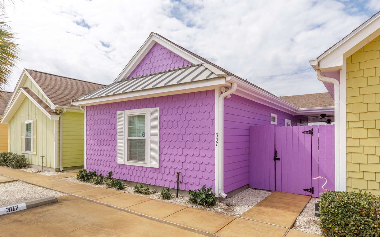 Bright purple cottage with cheerful yellow neighbors creates a vibrant beachside community setting.
