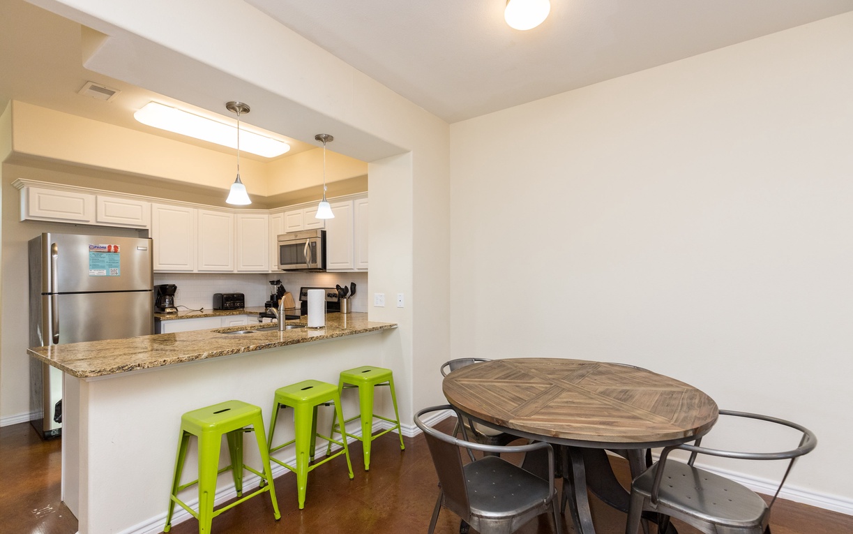 Your open-concept space seamlessly blends cooking and dining with granite counters, bright green stools, and a rustic round table for memorable meals.
