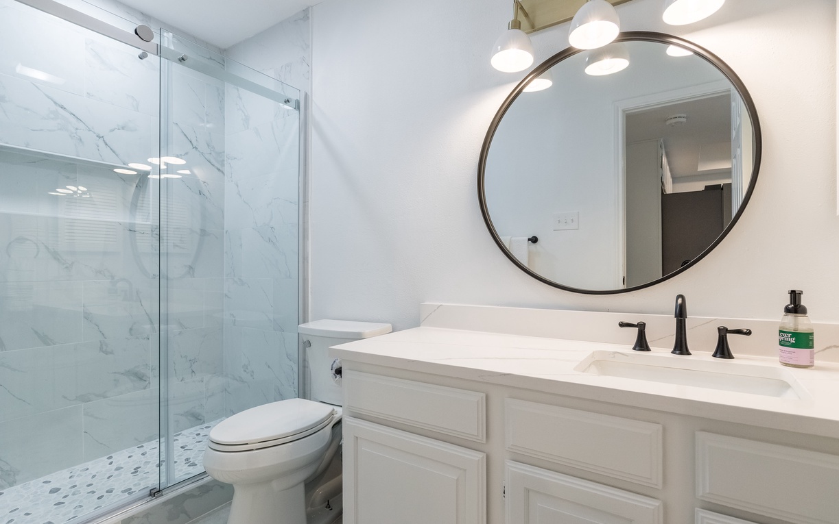 Step into your pristine bathroom featuring marble-inspired finishes, a spacious glass shower, and elegant vanity with warm lighting for your comfort.