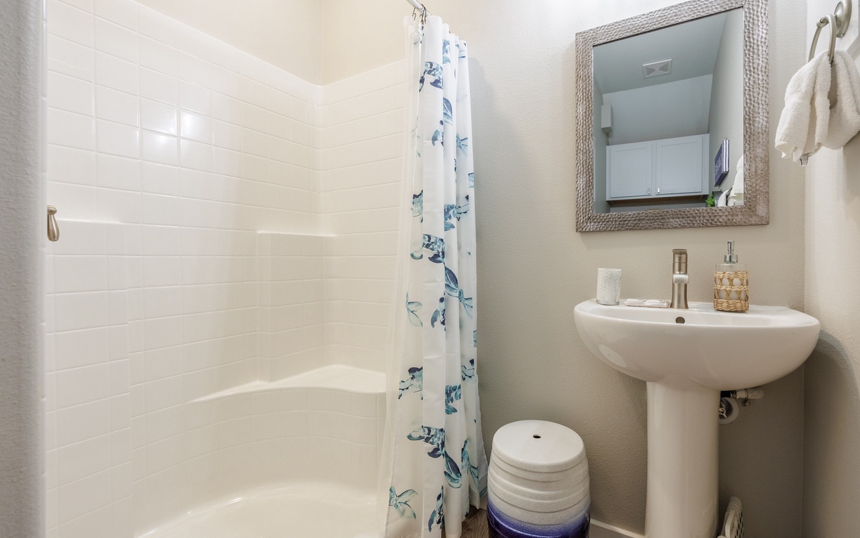 Your pristine bathroom features a refreshing shower with coastal-themed curtain, modern sink, and thoughtfully appointed amenities for your comfort.