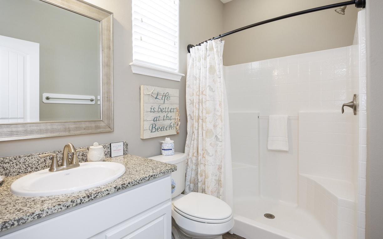 Refresh in your pristine bathroom with granite counters, beach-themed decor, and a spacious shower featuring crisp white tile.