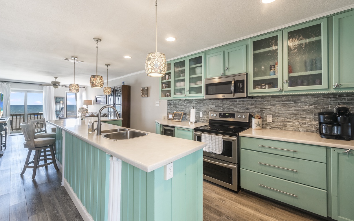 Your fully equipped kitchen features sea-green cabinets and ocean views, perfect for cooking meals while watching waves roll in.